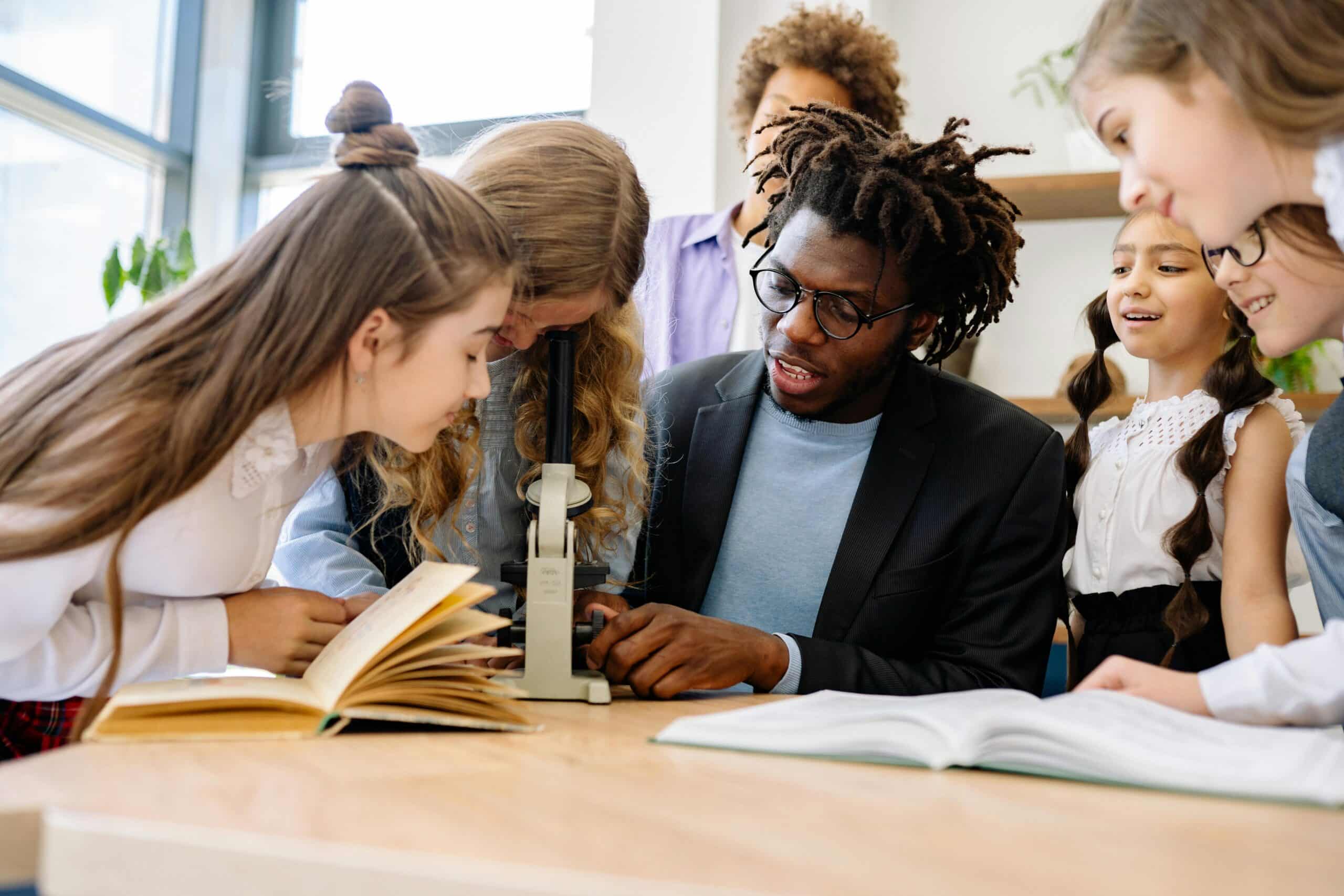 Christian school science teacher demonstrating microscope use to middle school students in a bright classroom, promoting academic integrity, faith integration, and hands-on STEM learning.
