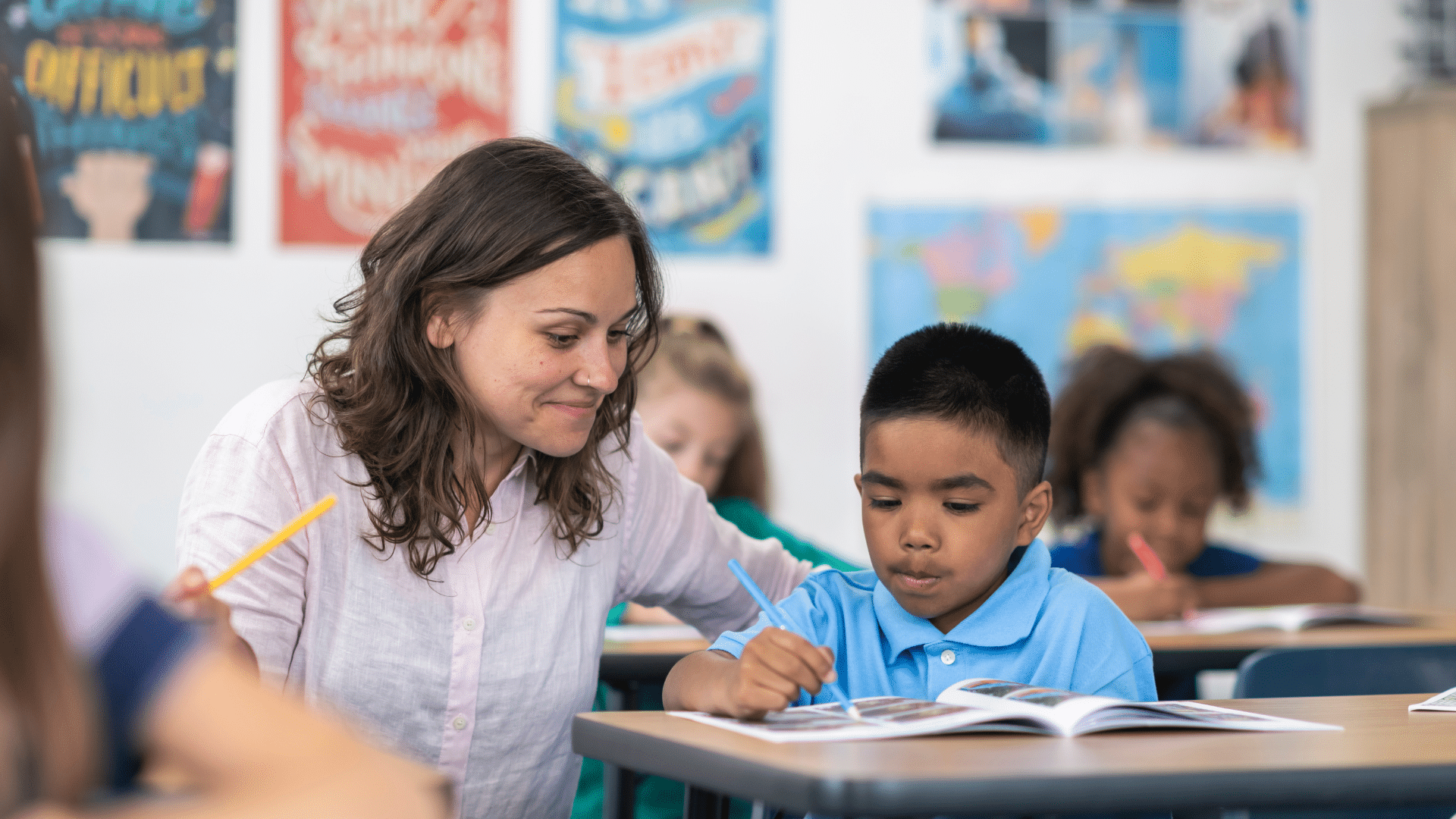 An image of a female teacher helping a student at his desk.