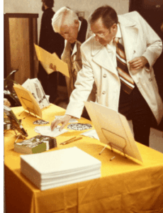 A photo of two guests at the 1979 NUCS building dedication peruse materials on a table.