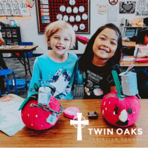 A photo of two students posing with a pumpkin craft on a school table.