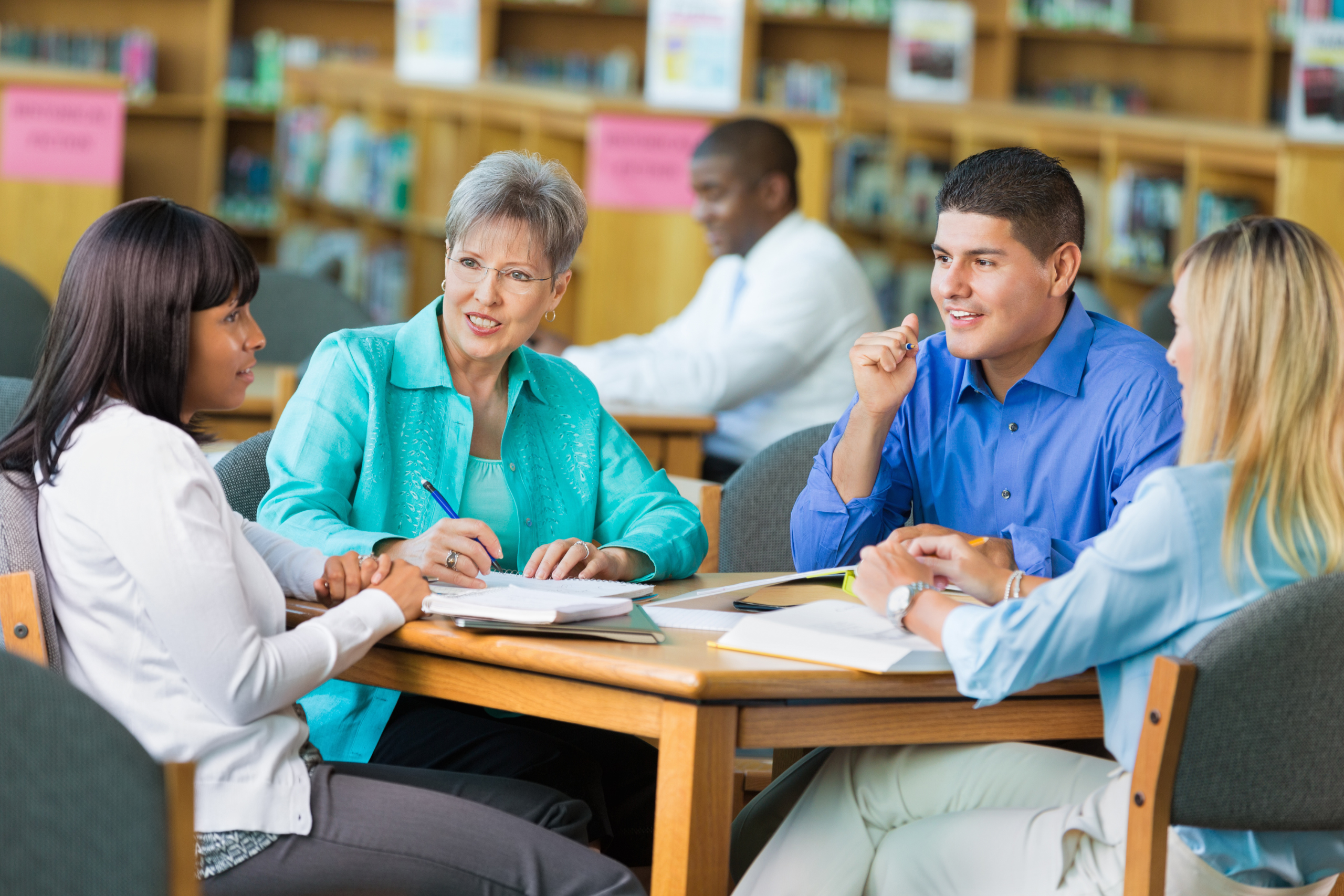 A group of teachers work together at a library table.
